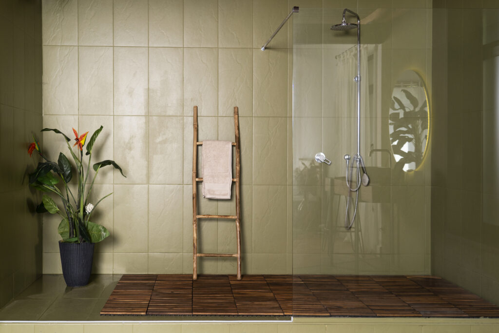 Modernes Badezimmer mit Glasdusche, hellgrünen Fliesen, Holzlattenboden, Bambusleiter mit Handtuch und Topfpflanze