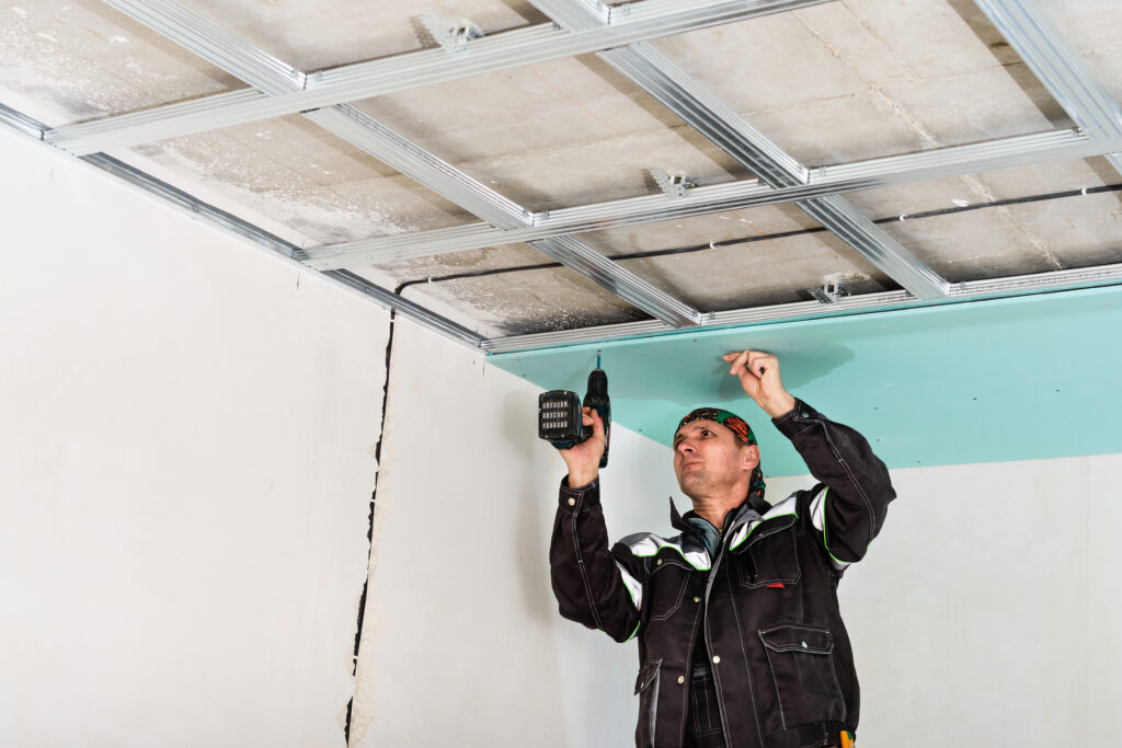 Handwerker befestigt Gipskarton an Decke mit Akku-Bohrschrauber in Metallunterkonstruktion